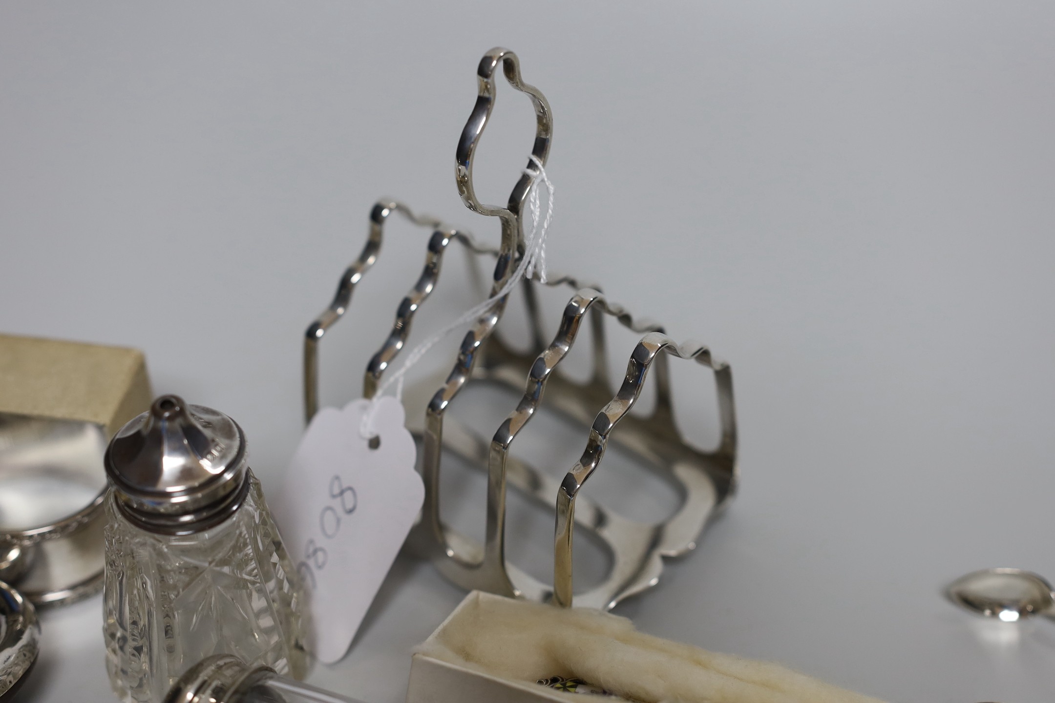 Assorted minor silver ware including a George V toast rack by James Dixon & Sons, 86mm, two napkin rings, a mounted glass toilet jar and condiment, pair of sugar tongs, a fruit knife, a commemorative spoon, a mounted sma